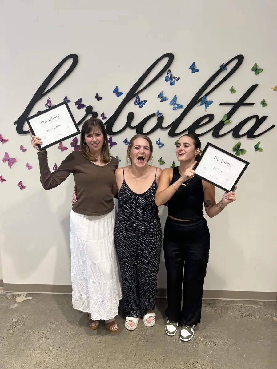Mary J with two Pro Artistry course graduates holding their certificates in front of a Borboleta wall